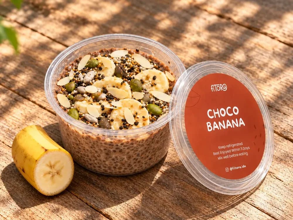 Chia Pudding Choco Banana dengan pisang dan biji-bijian, tutupnya di samping, di meja kayu bermatahari