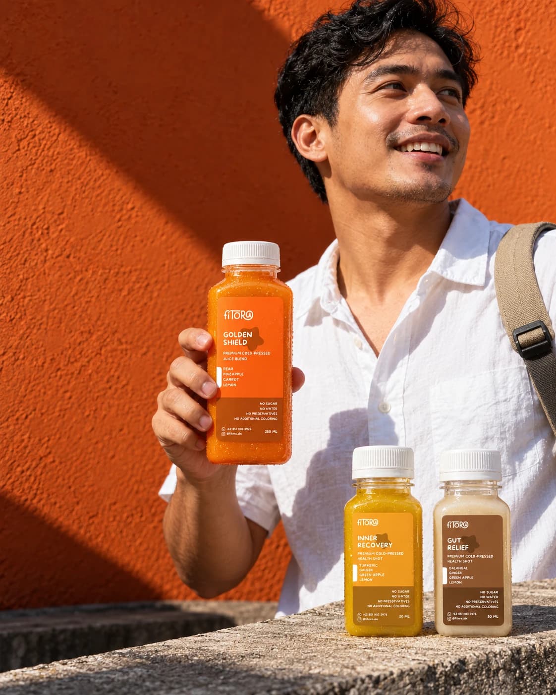 Laki-laki berkemeja putih tersenyum memegang Golden Shield, dengan shot Inner Recovery dan Gut Relief di tepi beton.